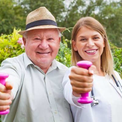 Smiling female therapist doing strength exercises with dumbbell with elderly male patient in the park